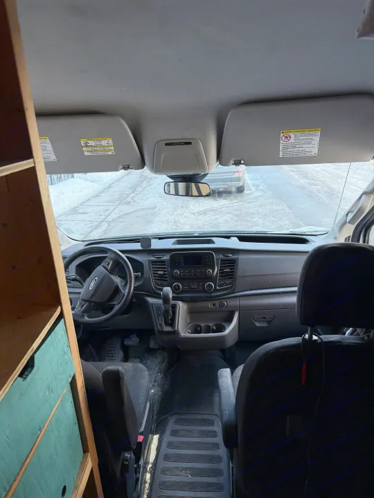 RV rental: Interior of a Ford Transit camper van, showing the driver's cabin with steering wheel, dashboard, and custom shelves.. Ford Transit 2021