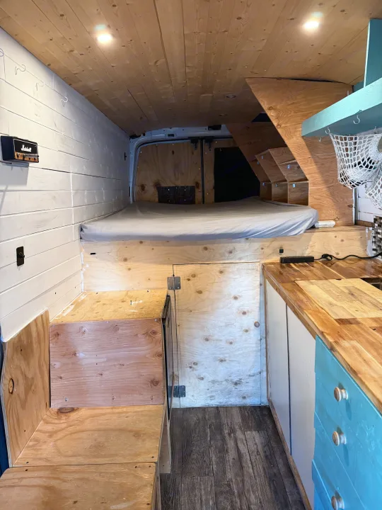 Cozy wood-paneled RV rental interior featuring a bed, kitchenette, and smart storage solutions for adventurous travel.. Ford Transit 2021