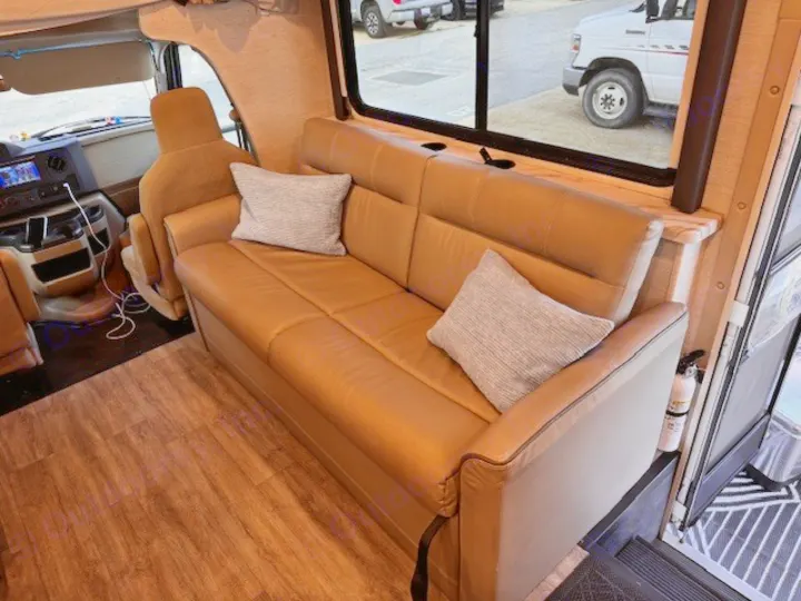 Comfortable RV rental living area with a plush tan sofa, wood-look floor, and accessible cabin view for your next adventure.. Thor Four Winds 2025