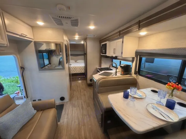 Bright rv rental interior showing dining area, kitchen with coffee maker, and cozy couch; leads to a rear bunk room.. Thor Four Winds 2025