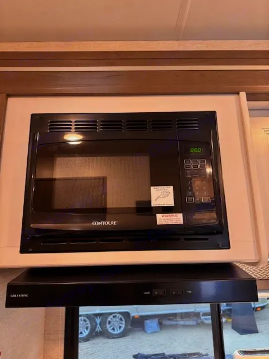RV rental kitchen showcasing a black Contoure microwave oven over a Greystone range hood, ready for use on the road.. Thor Four Winds 2025
