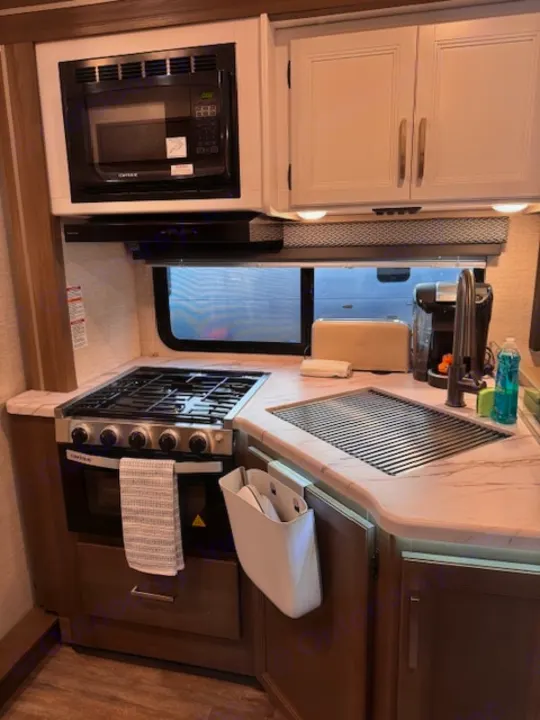 Compact RV rental kitchen featuring a microwave, gas stove, sink with drying rack, coffee maker, toaster, and cabinets.. Thor Four Winds 2025
