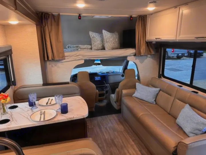 Spacious RV rental interior featuring a dinette, sofa, and overhead bunk bed, designed for comfortable travel.. Thor Four Winds 2025
