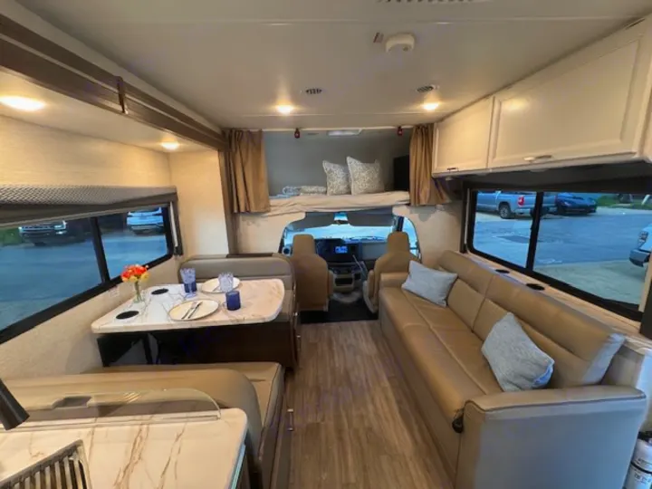 Inside a modern RV rental: neutral-toned dinette, couch, overhead bed, and storage for comfortable travel.. Thor Four Winds 2025