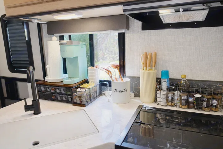 Neat RV rental kitchen: mint Keurig, paper towels, knife block, and spice rack on a marbled counter by the sink & stove.. Cruiser RV Radiance Ultra Lite 2020