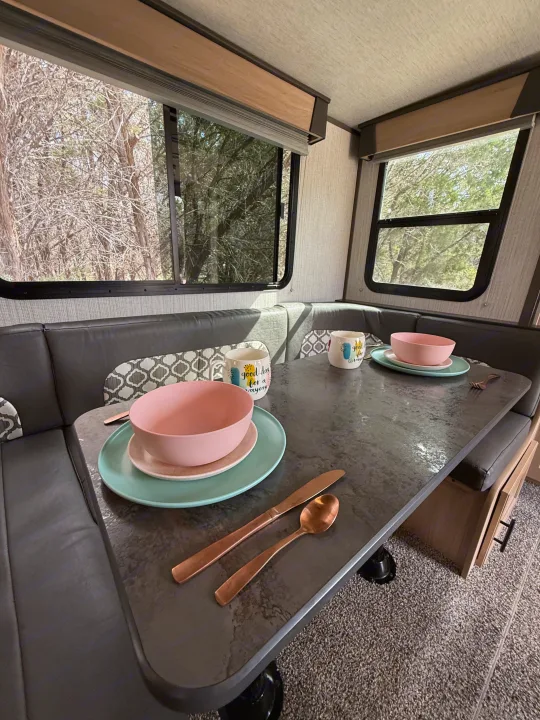 Cozy RV rental dinette set for two with pink & mint tableware and mugs, offering a lovely view of the trees outside.. Cruiser RV Radiance Ultra Lite 2020