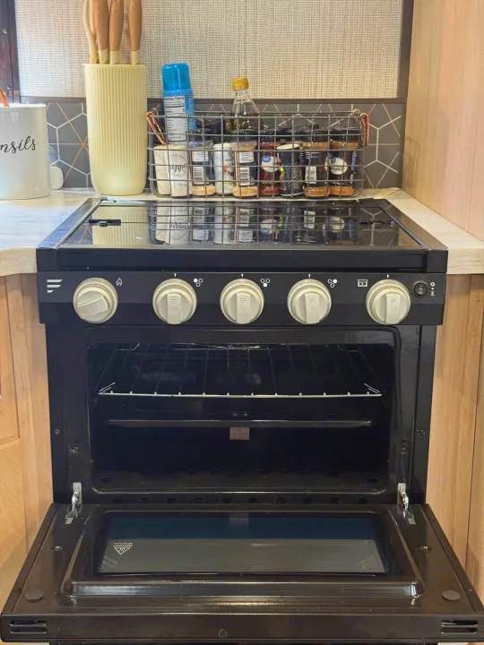 RV rental kitchen featuring a black stove/oven with an open door, revealing racks, and a counter with spices and utensils.. Cruiser RV Radiance Ultra Lite 2020