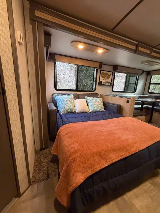 Cozy RV rental interior with sofa bed, dinette, colorful pillows, and bright windows showing a forest view.. Cruiser RV Radiance Ultra Lite 2020