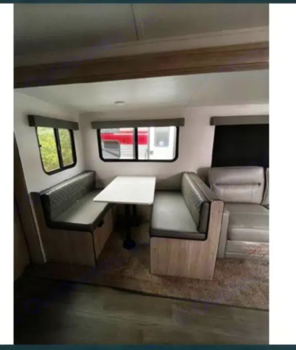 RV rental interior showcasing a cozy dinette with bench seats and a sofa seating area, illuminated by natural light from windows.. Riverside RV Intrepid 2023