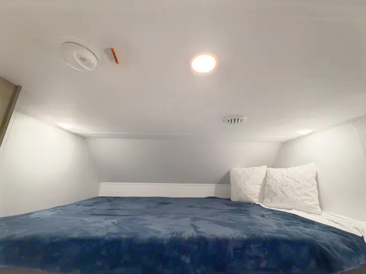 Cozy rv rental bunk: a dark blue bed with white pillows, overhead lighting, a smoke detector, and an air vent.. Forest River Sunseeker LE 2025