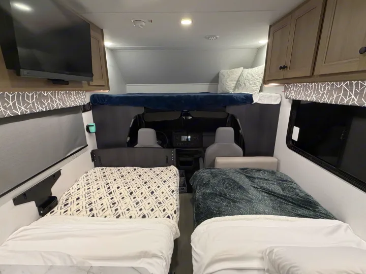 Interior of an RV rental, featuring two twin beds, an overhead bunk sleeping area, and the front cab.. Forest River Sunseeker LE 2025