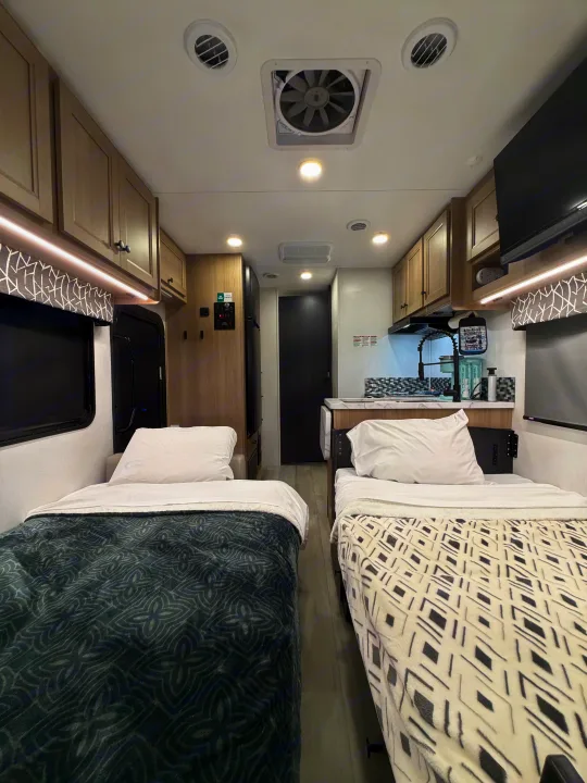 Well-equipped RV rental interior showing two beds, kitchen area, overhead storage, and bright lighting.. Forest River Sunseeker LE 2025