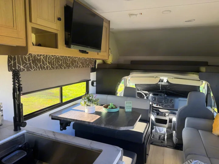 Bright RV rental interior showcasing a modern dinette, kitchen, overhead TV, and bunk. Ready for your next adventure!. Forest River Sunseeker LE 2025