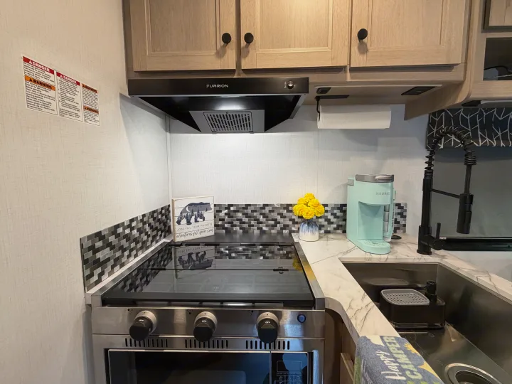 RV rental kitchen with stove, sink, Keurig, and decor, showing a compact yet functional design for travel and cooking.. Forest River Sunseeker LE 2025