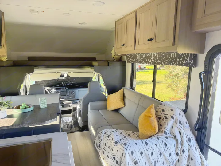 This inviting rv rental interior shows the living area, kitchen counter, cockpit, and overhead bed, perfect for travel.. Forest River Sunseeker LE 2025