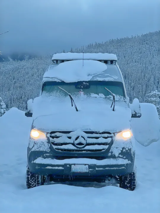 This Mercedes Sprinter RV rental, covered in snow, lights up a winter forest, ready for cold-weather adventures.. Mercedes-Benz Sprinter 2020