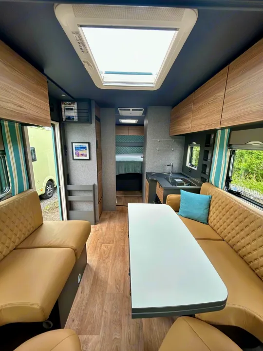 Explore this bright RV rental interior featuring a living area, kitchen, bedroom, and a large skylight in this cozy campervan.. GlamperRV DBL 2025