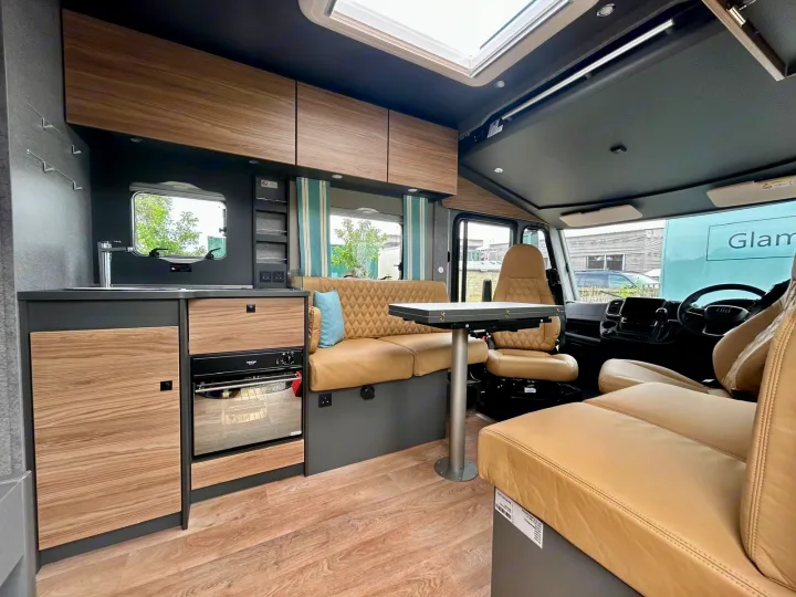 Modern rv rental interior: features a kitchen, dining area with tan seating, and overhead storage, perfect for comfortable mobile living.. GlamperRV DBL 2025