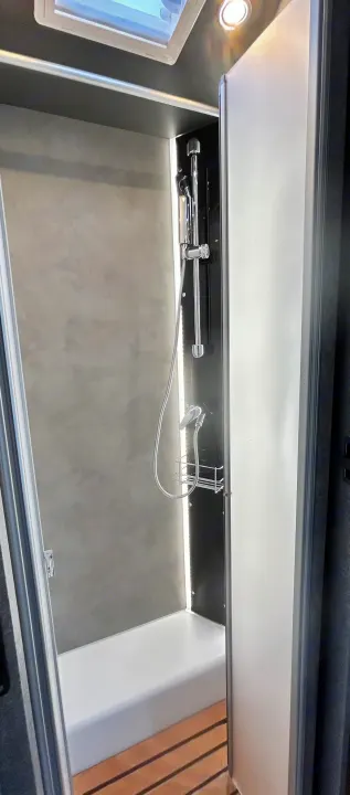 Modern RV rental shower with skylight, adjustable shower head, and sleek design. Perfect for your next adventure.. GlamperRV DBL 2025