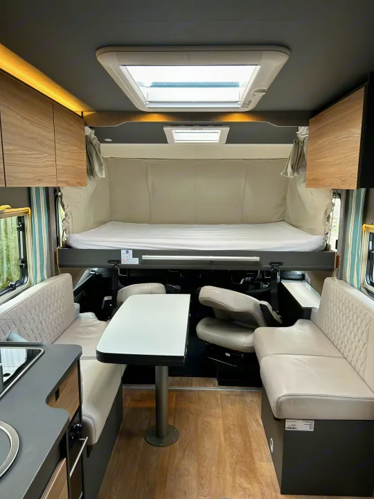 Bright rv rental interior showing a drop-down bed, dining table with bench seating, and a modern kitchen unit for road trips.. GlamperRV DBL 2025
