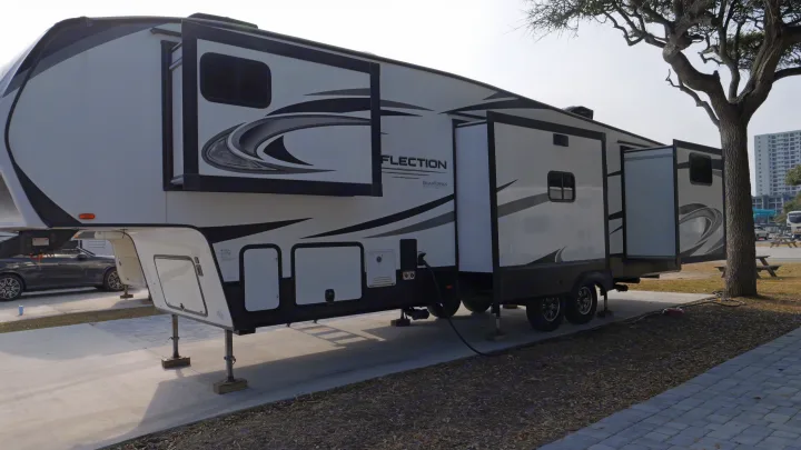 Large white and black fifth-wheel RV rental with slide-outs extended, parked at a paved campsite.. Grand Design Reflection 2022