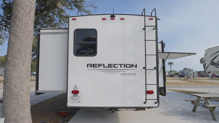 Rear of a white Grand Design Reflection travel trailer, with a slide-out and ladder. Great for your next rv rental adventure!. Grand Design Reflection 2022