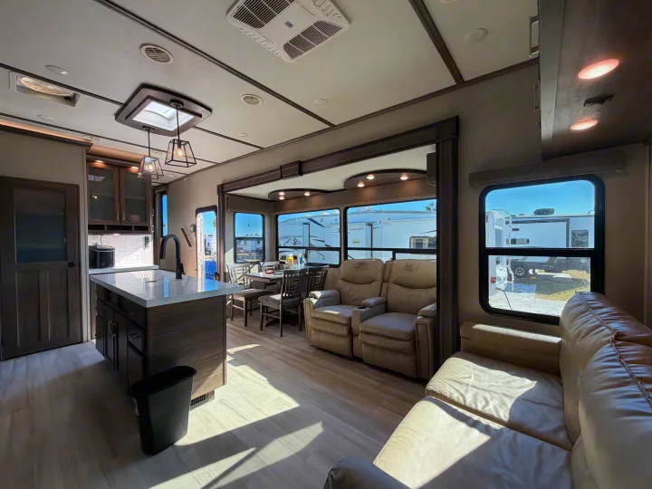 Spacious RV rental interior featuring a kitchen island, dining area, recliners, and light wood floors, bathed in natural light.. Grand Design Solitude 2021