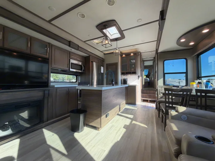 Bright, modern RV rental interior showing a kitchen, living area with fireplace, and dining table. Sunlight casts long shadows.. Grand Design Solitude 2021