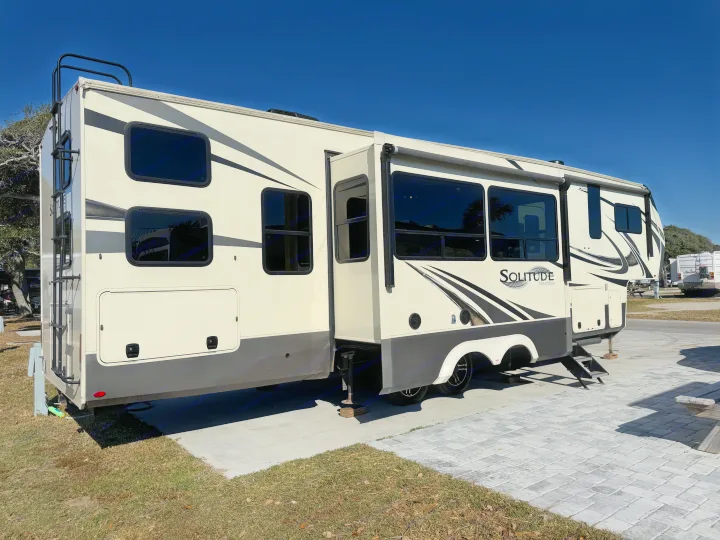 Experience travel in this spacious Grand Design Solitude fifth-wheel RV rental, parked on a sunny campsite with slide-outs extended.. Grand Design Solitude 2021