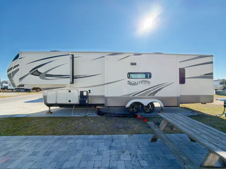 Solitude Grand Design fifth-wheel RV rental parked at a sunny campsite with slides extended, utility hookups & picnic table.. Grand Design Solitude 2021