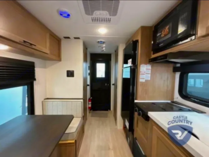 Bright RV rental interior: well-equipped kitchen with stove, microwave, and fridge, plus a dining booth. Ample cabinets for storage.. Forest River Cherokee Wolf Pup 2023