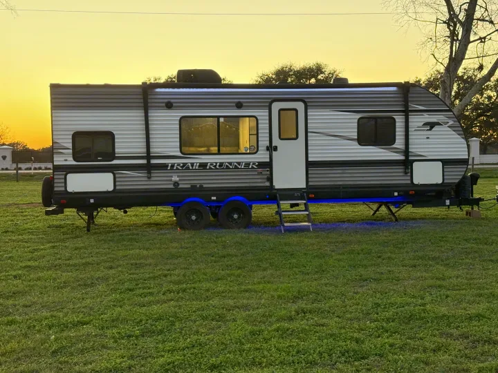 RV rental: A Trail Runner travel trailer with blue undercarriage lights in a grassy field at sunset.. Heartland RVs Trail Runner 2022