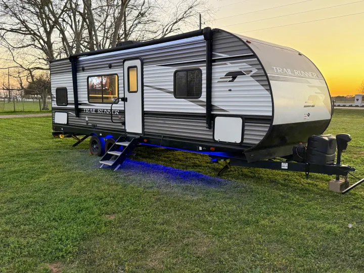 This sleek Trail Runner RV rental, lit with blue underglow, awaits its next adventure in a grassy setting at sunset.. Heartland RVs Trail Runner 2022