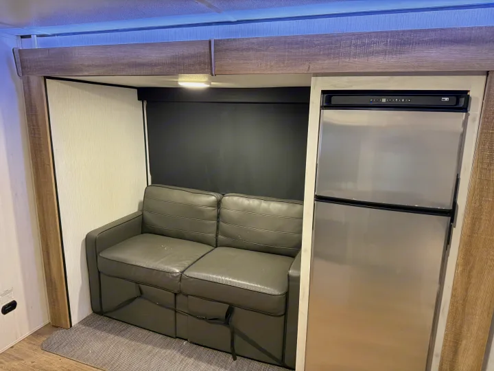 Cozy RV rental interior featuring a gray sofa, compact refrigerator, and overhead lighting for efficient living.. Heartland RVs Trail Runner 2022