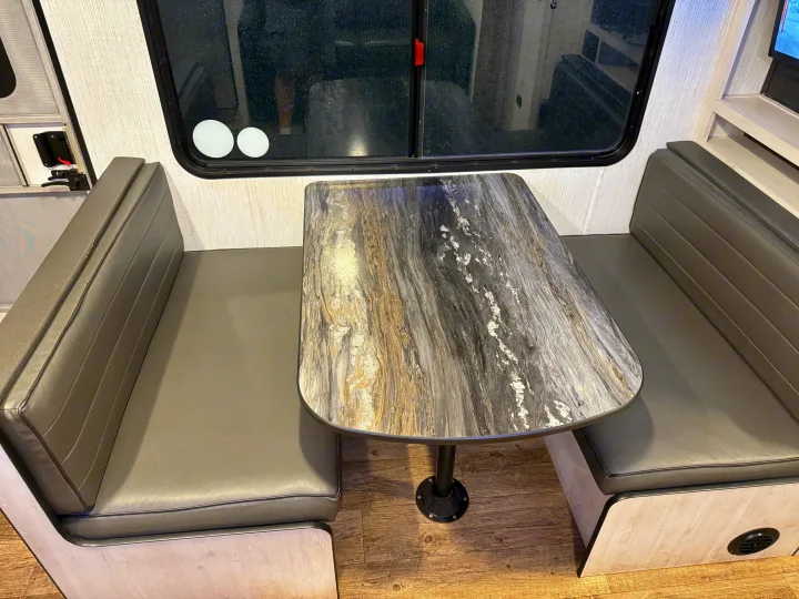 Functional RV rental dinette with grey cushioned benches and a stylish patterned table by the window.. Heartland RVs Trail Runner 2022