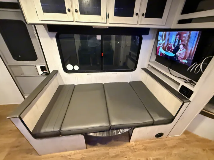 Modern RV rental interior: gray convertible dinette bed, large window, TV, and white overhead cabinets.. Heartland RVs Trail Runner 2022