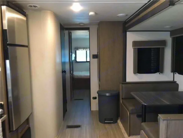 Inside an RV rental featuring a stainless steel fridge, a hallway leading to a bedroom, and a cozy dinette area.. Keystone RV Hideout 2021