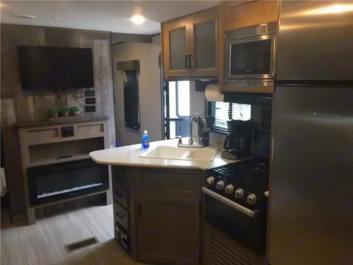 Explore this modern RV rental's interior, showcasing a fully equipped kitchen with stove, microwave, and fridge, plus a living area with TV and fireplace.. Keystone RV Hideout 2021