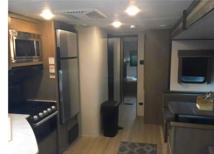 This rv rental interior features a kitchen with microwave, stove, and fridge, a dinette, and a hall leading to bunk beds.. Keystone RV Hideout 2021