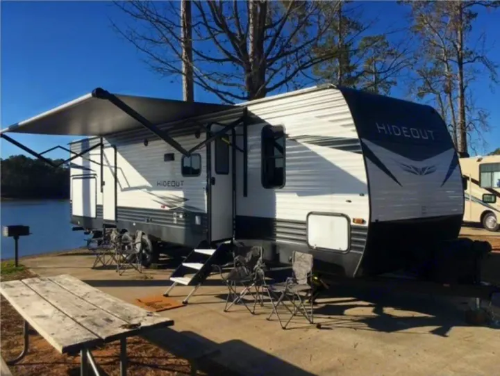 RV rental: Hideout travel trailer at a sunny lakeside campsite. Awning extended, with picnic table & chairs.. Keystone RV Hideout 2021