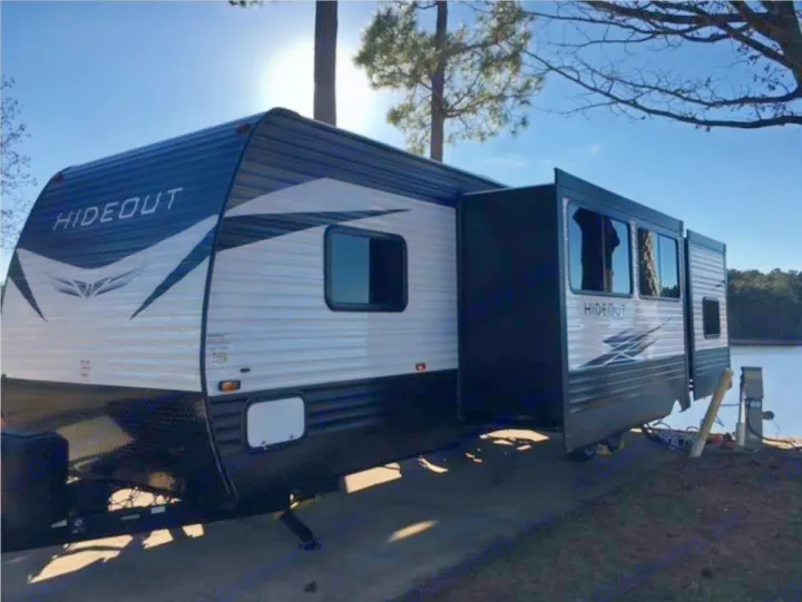 Waterfront RV rental: A Hideout travel trailer with slide-out extended, parked by a lake under sunny skies.. Keystone RV Hideout 2021