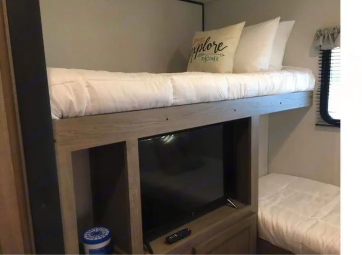 Bright RV rental interior featuring bunk beds with clean white bedding, a TV, and a cozy sleeping area.. Keystone RV Hideout 2021
