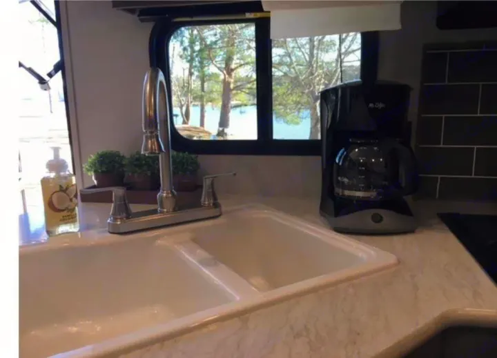 Inside an RV rental kitchen: white double sink, chrome faucet, coffee maker, and a scenic lake view from the window.. Keystone RV Hideout 2021