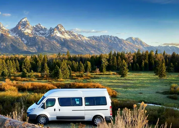 White RV rental at Grand Teton NP, parked before majestic snow-capped mountains, dense forest, and grassy plains.. Thor Scope 2024