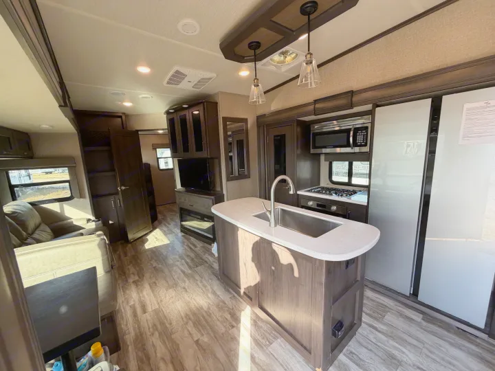 Modern rv rental interior features a full kitchen with island, stove, and fridge, plus a cozy living room with TV and recliners.. Grand Design Reflection 2022