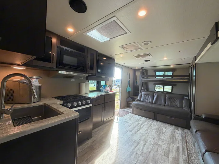 Spacious RV rental interior featuring a modern kitchen with stove, microwave, sink, and a comfortable living area with bunk beds.. Grand Design Transcend 265BH 2022