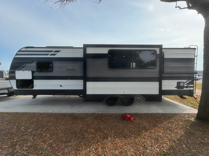 A black, white, and grey Transcend Xplor travel trailer RV rental with its slide-out extended, parked on a concrete pad.. Grand Design Transcend 265BH 2022