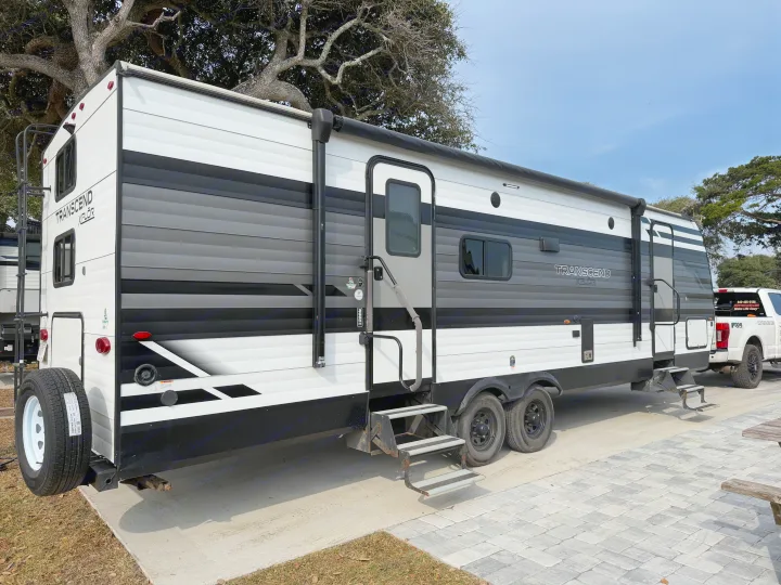 A white and gray Transcend Xplor rv rental travel trailer parked with an attached pickup truck, ready for outdoor adventures.. Grand Design Transcend 265BH 2022