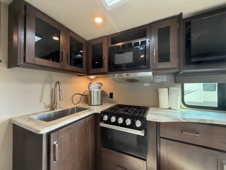 Compact RV rental kitchen with dark cabinets, modern sink, stove, microwave, and ample counter space.. Grand Design Transcend 265BH 2022