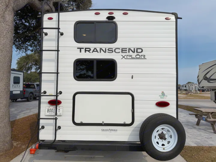 Rear of a white Transcend XPLOR **rv rental** at a campground, featuring a ladder, spare tire, and a South Carolina license plate.. Grand Design Transcend 265BH 2022